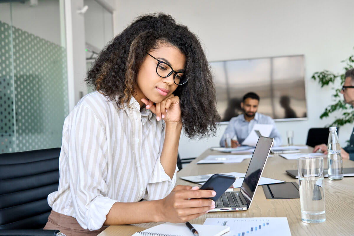 Szemüveges nő ül egy mobiltelefon segítségével